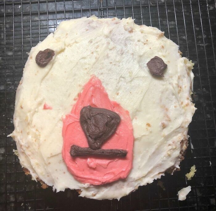 Cursed and disgusting food picture of a poorly frosted cake with odd chocolate and pink icing face design.