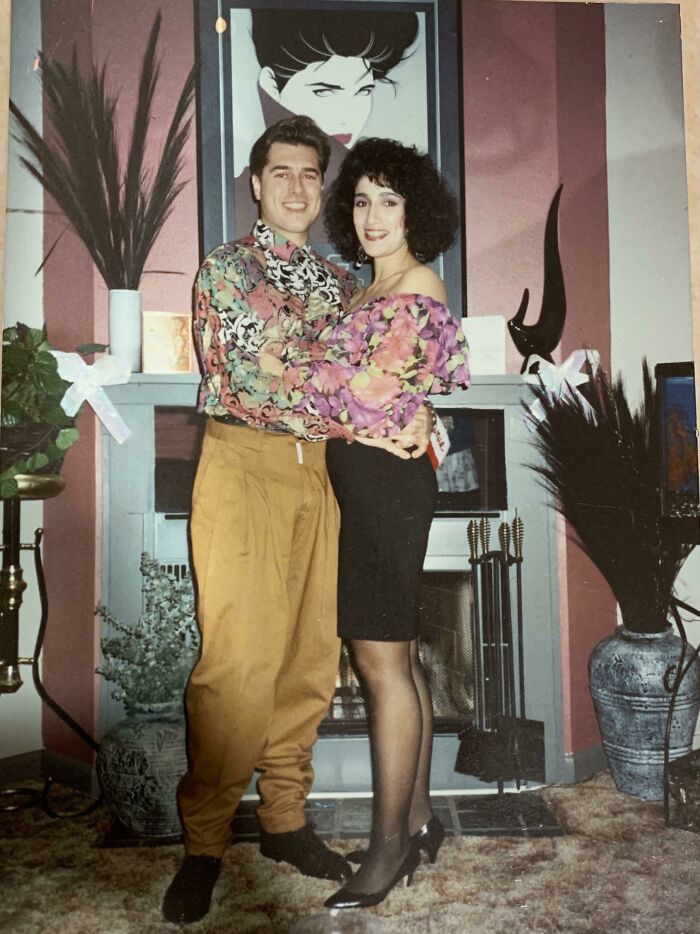 Couple dressed in colorful 1980s fashion posing at home with floral patterns and bold style showing wild and wonderful 80s vibe.