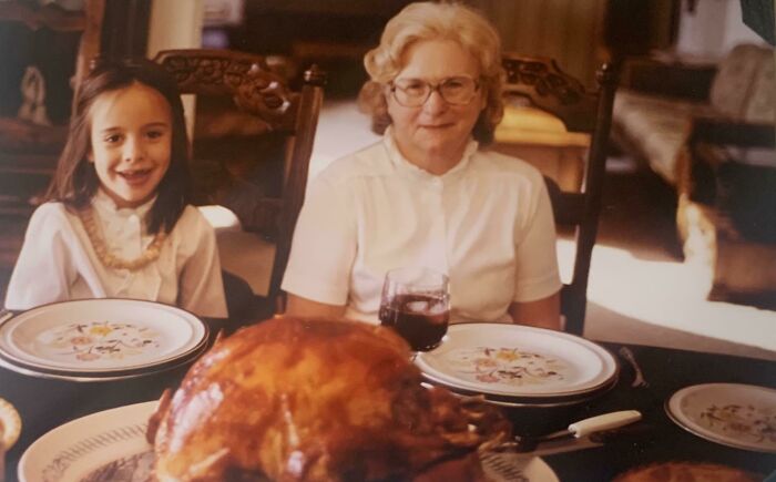Grandmother and granddaughter smiling at the dinner table with a roasted turkey, capturing 1980s family moments.
