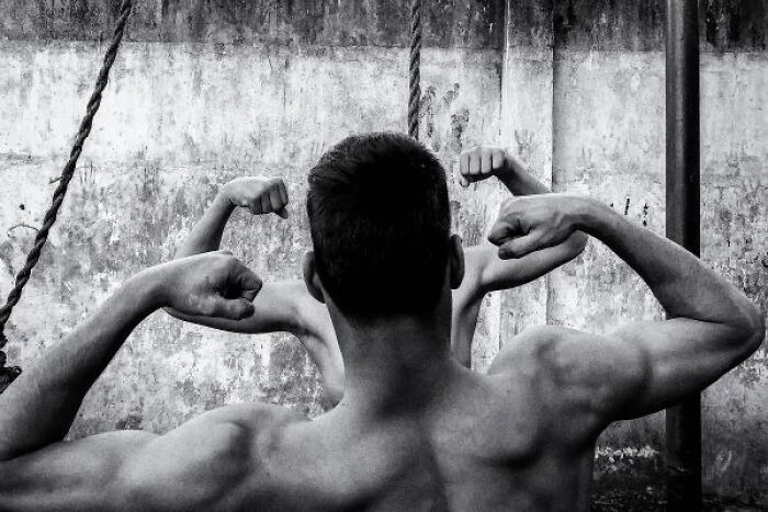 Black-and-white photo of muscular men flexing their arms on the streets of India, showcasing strength and urban life.