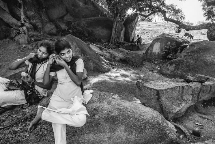 Two young women adjusting earrings outdoors on rocky terrain in a black-and-white street photo from India.
