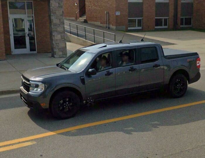 A gray pickup truck with two blurred occupants parked outside a building seen in Google Earth unexpected capture.