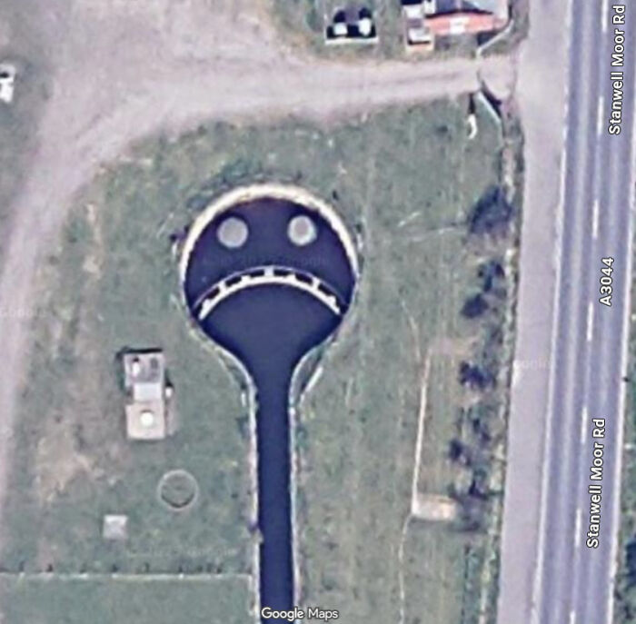 Aerial view of a sad face shape formed by water and structures, an unexpected capture on Google Earth and Maps.