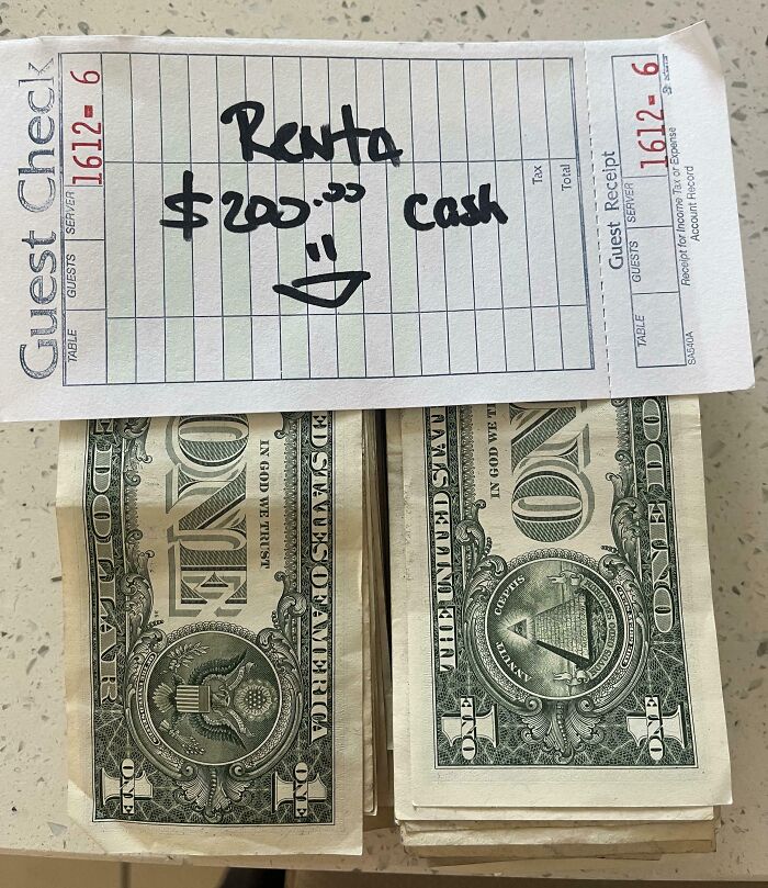 Stack of one-dollar bills with a handwritten note on a guest check saying rent $200 cash, a mildly infuriating sight.