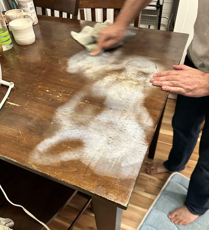 Person scrubbing a wooden table with a worn, discolored patch, showing mildly infuriating things testing patience.