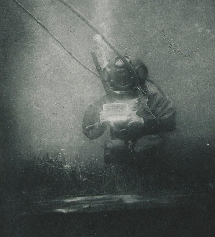 Underwater diver in vintage diving suit holding an object, one of the rare photos from early photography era.