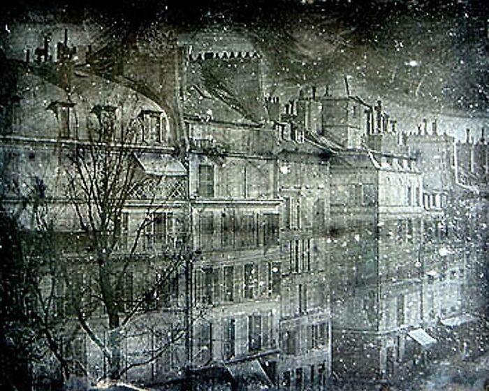 Early black and white photograph of snow falling on old buildings, capturing a moment from photography's early days.