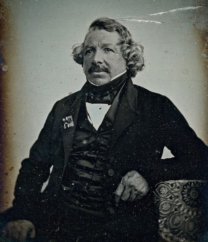 Vintage portrait of a man with curly hair, dressed formally, from the time when photography was a new phenomenon.