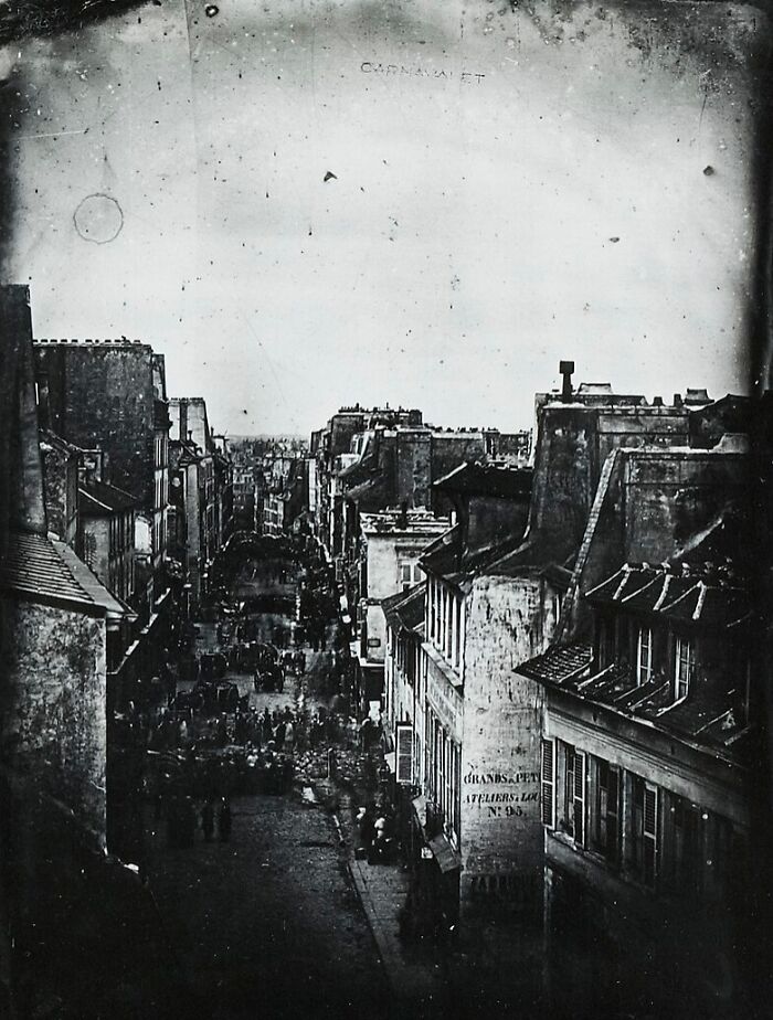 Black and white early photograph of a crowded city street showcasing vintage architecture and people from the early days of photography.