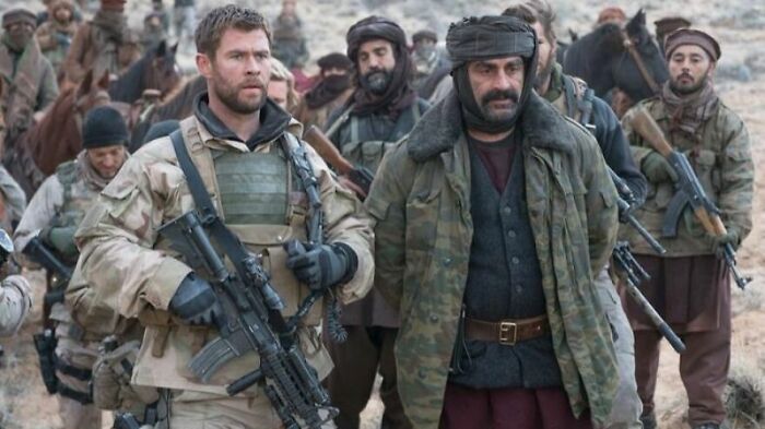 Soldiers and locals in military gear walking together in a scene from movies based on true stories.