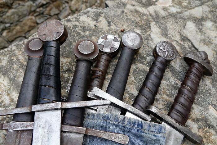 Collection of Viking swords with detailed hilts laid on stone, showcasing historical Viking weaponry and craftsmanship.
