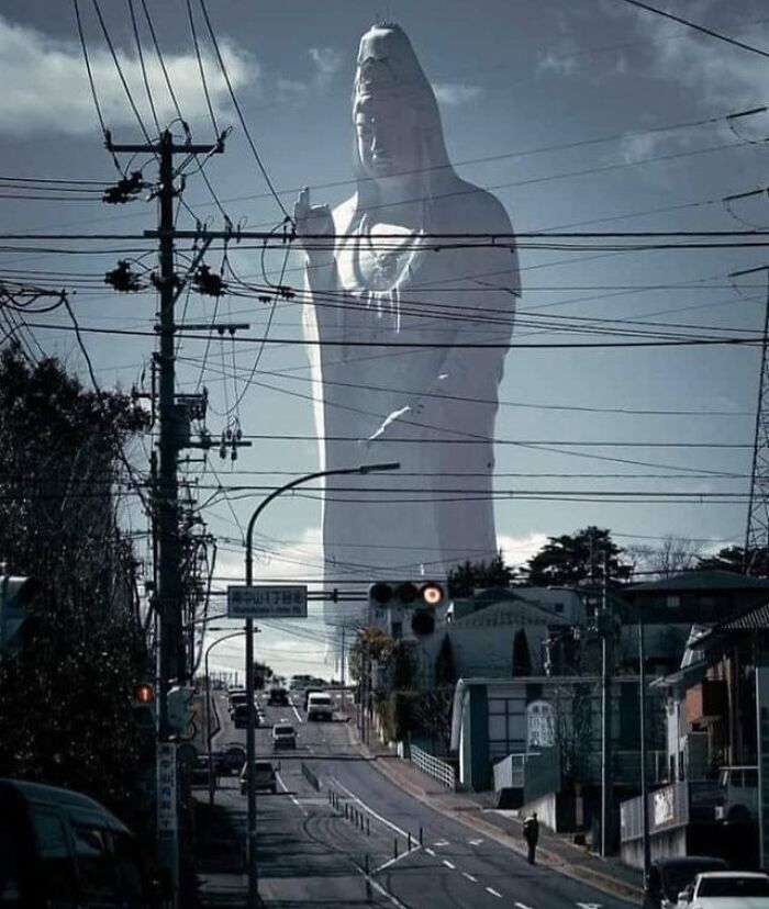 Giant statue towering over an urban street with power lines, creating a beautiful yet unnerving liminal space.
