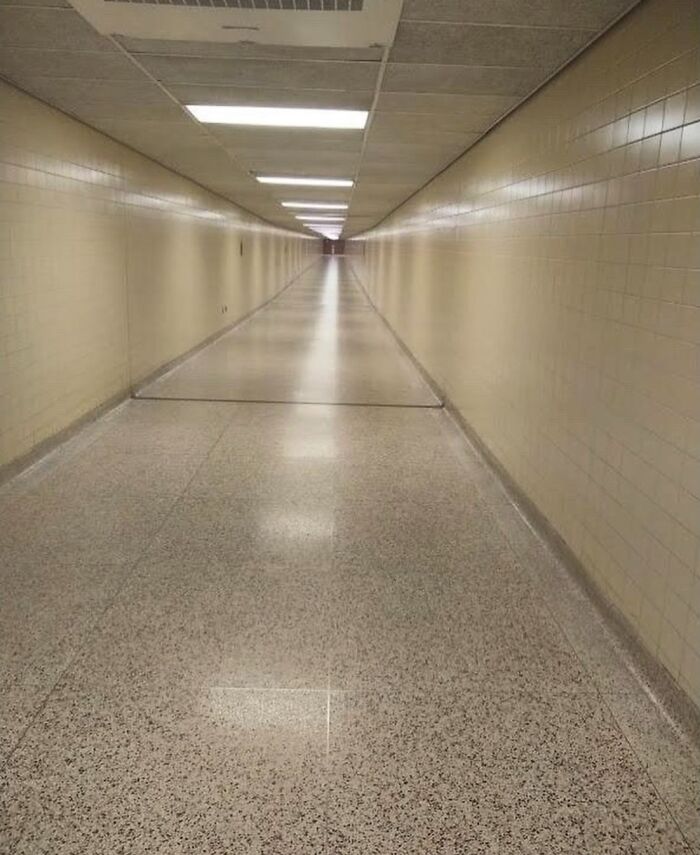 Long empty liminal hallway with beige walls and ceiling lights, creating a beautiful yet unnerving atmosphere.