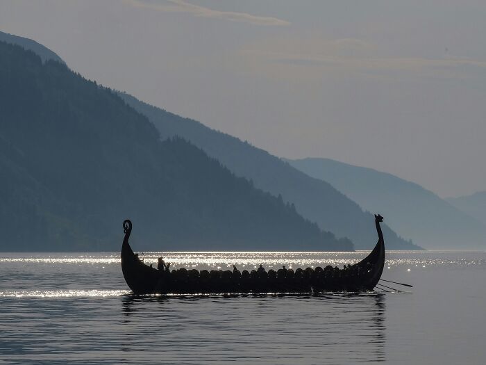 Viking ship silhouette on calm water with mountainous landscape in the background, representing Viking facts and history.