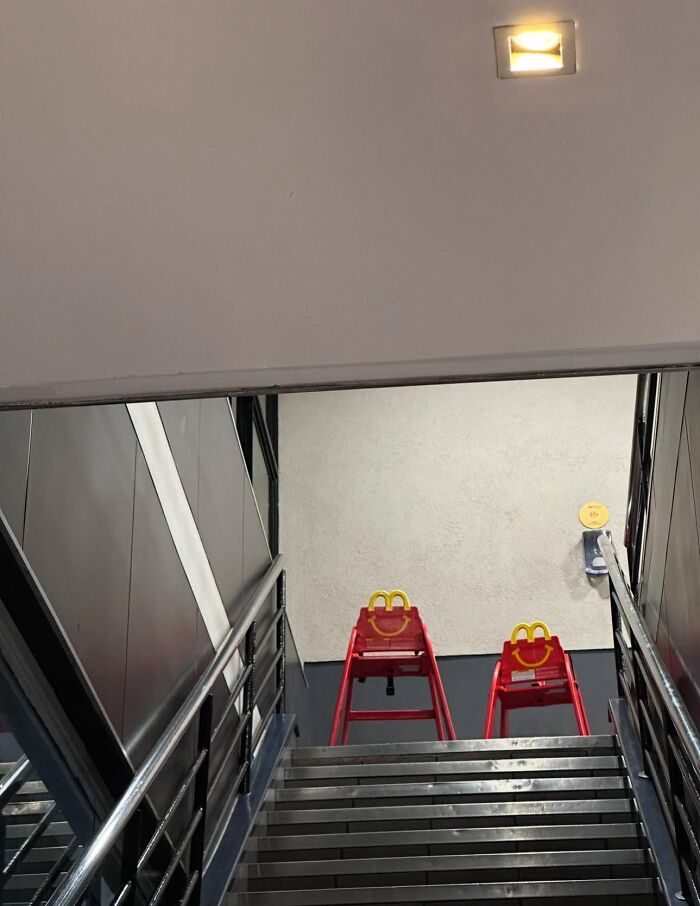 Staircase view of two red McDonald's high chairs in a liminal space with metal railings and plain walls.