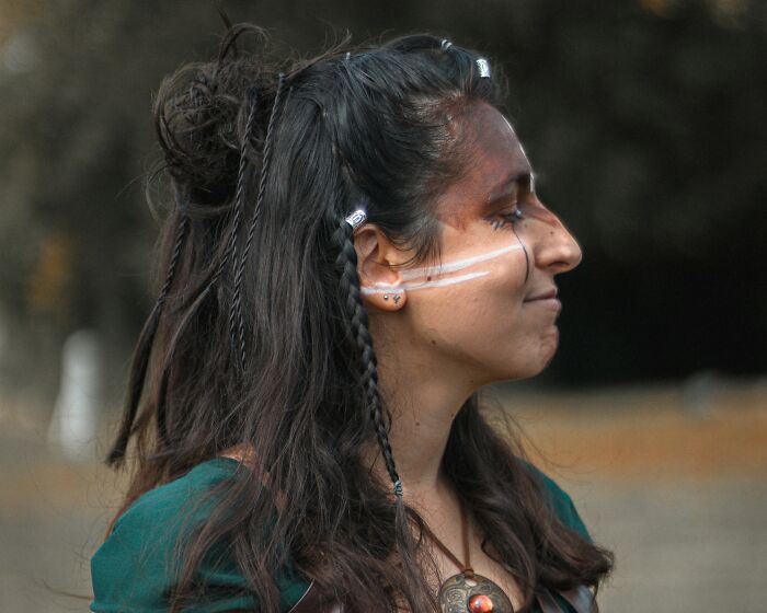 Woman with braided hair and tribal face paint outdoors, representing Viking culture and lifestyle in historical reenactment.