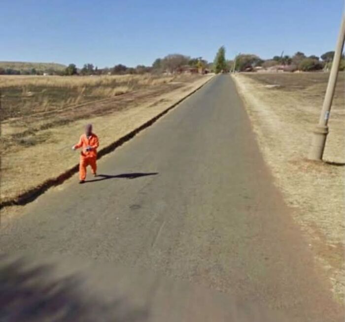 Child in an orange outfit walking alone on a rural road, an unexpected moment captured on Google Earth and Maps.