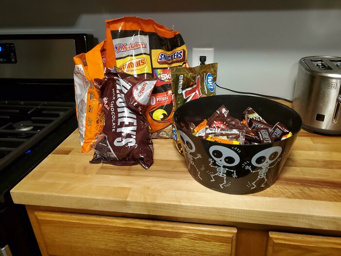 Assorted Halloween candy bags and a skeleton-themed bowl partially filled with candy on a kitchen countertop.