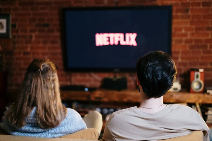 Two people sitting on a couch watching Netflix on TV, illustrating frustrating workplace rules impact on downtime.