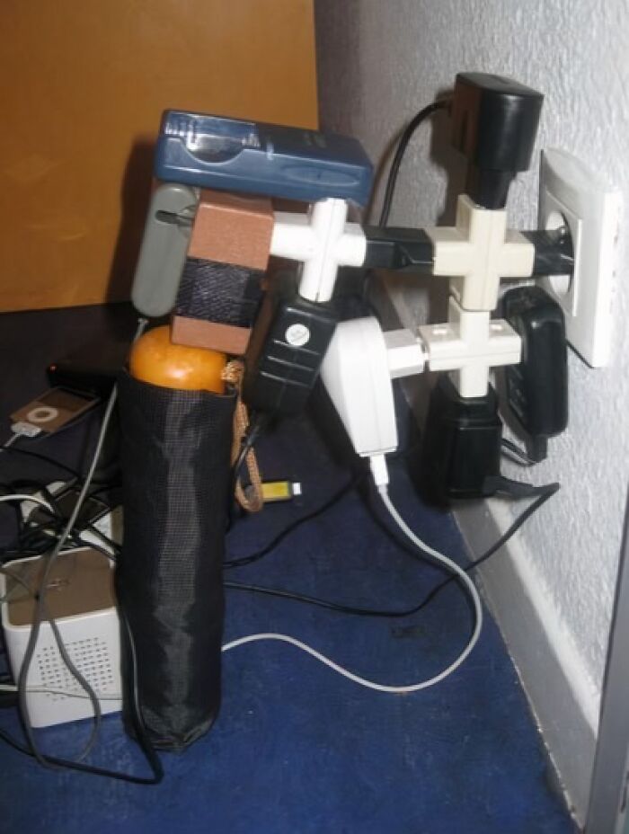 Overloaded power strip supported by an orange and tape in a risky and incorrect electronics handling setup.