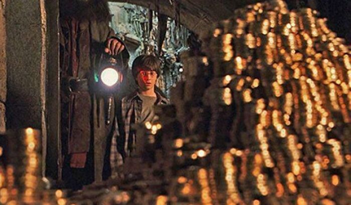 Boy with glasses holding a lantern in a dark cave filled with stacks of gold coins in bad movie details group discussion.