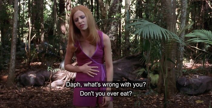 Woman in a purple dress in a forest scene from a bad movie with confusing details and subtitles about eating.