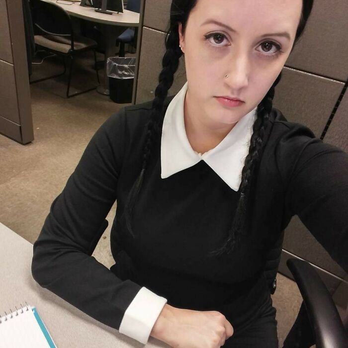 Person dressed in a black dress with white collar and cuffs, resembling a Halloween fail costume at an office desk.