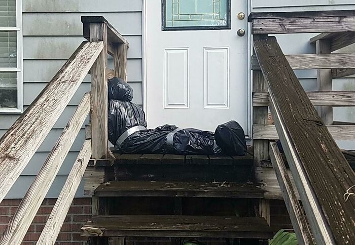 Halloween fail with a taped black plastic figure awkwardly placed on wooden stairs outside a house.