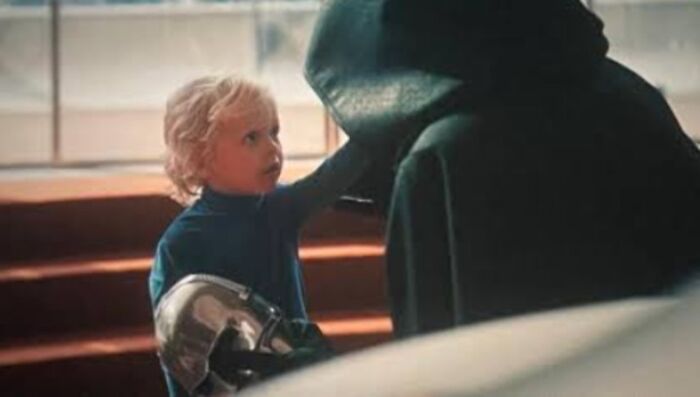 A young child with a metal arm touching a cloaked figure, highlighting confusing bad movie details in a dramatic scene.