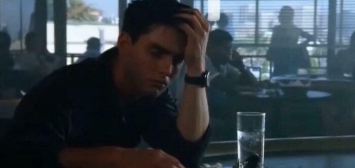 Young man in a dark shirt sitting at a table looking confused, illustrating bad movie details in an online group discussion.