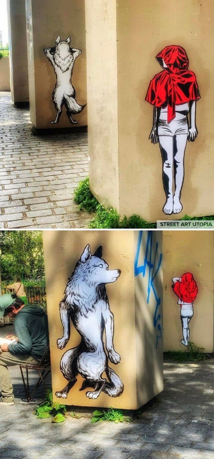 Street art showing a girl in a red hood and a wolf painted on outdoor beige pillars in an urban setting.