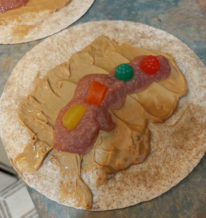 Peanut butter spread on a tortilla topped with raw ground meat and colorful gummy candies in a bizarre food combination.