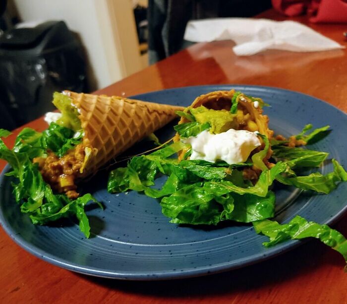 Two waffle cones filled with lettuce, guacamole, and sour cream on a blue plate, showing cursed and disgusting food combination.
