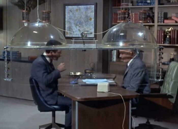 Two men in suits sitting at a retro office desk under vintage plastic dome lights, nostalgic scene making people feel very old.