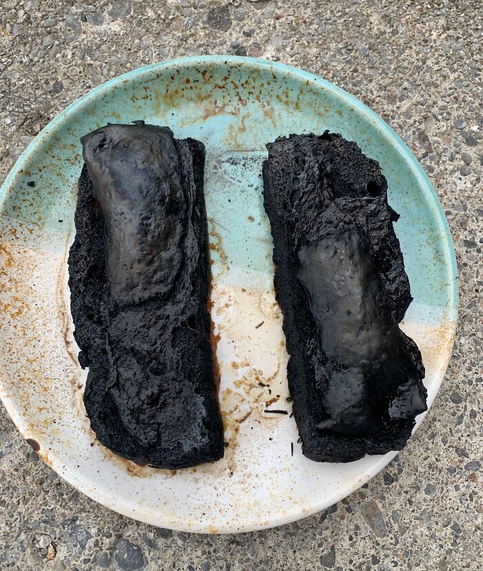 Burnt, blackened slices of bread with charred toppings on a stained plate, showing cursed and disgusting food appearance.