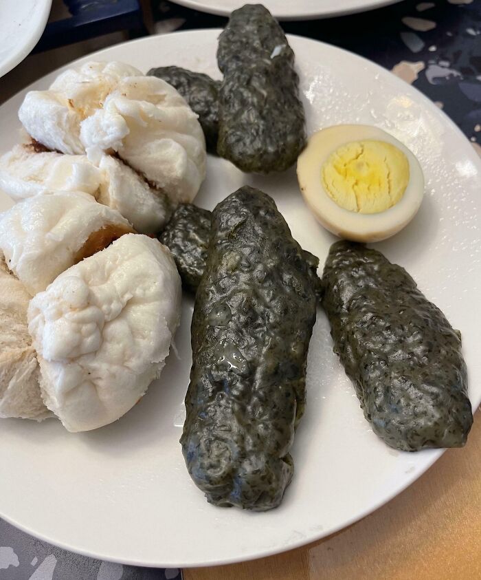 Plate with dark green cursed food resembling pickles, steamed buns, and a halved boiled egg, showcasing disgusting pictures of food.