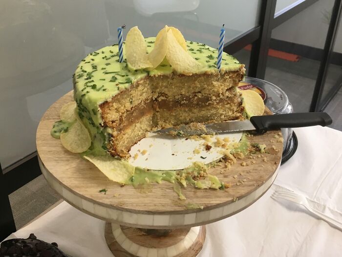 Half-eaten cake with green sauce and potato chips on top, displayed on a wooden cake stand, a cursed food picture.