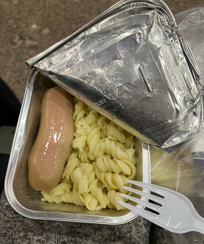 Cursed and disgusting food picture showing unappetizing pale sausage and overcooked pasta in a foil container with plastic fork.