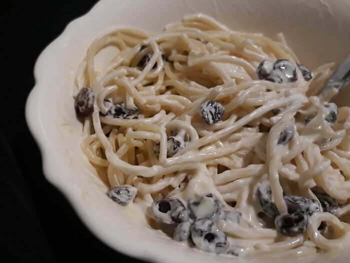Bowl of creamy spaghetti with raisins, an unusual and cursed food combination that looks unappetizing and disgusting.