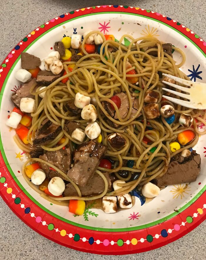 Plate of spaghetti mixed with marshmallows, candy pieces, and chocolate chunks, a cursed and disgusting food combination.