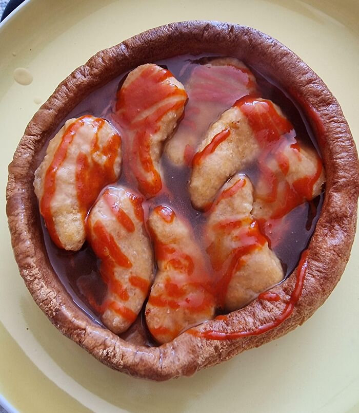 Close-up of a cursed and disgusting food dish with chicken nuggets in a soggy bread bowl topped with red sauce.