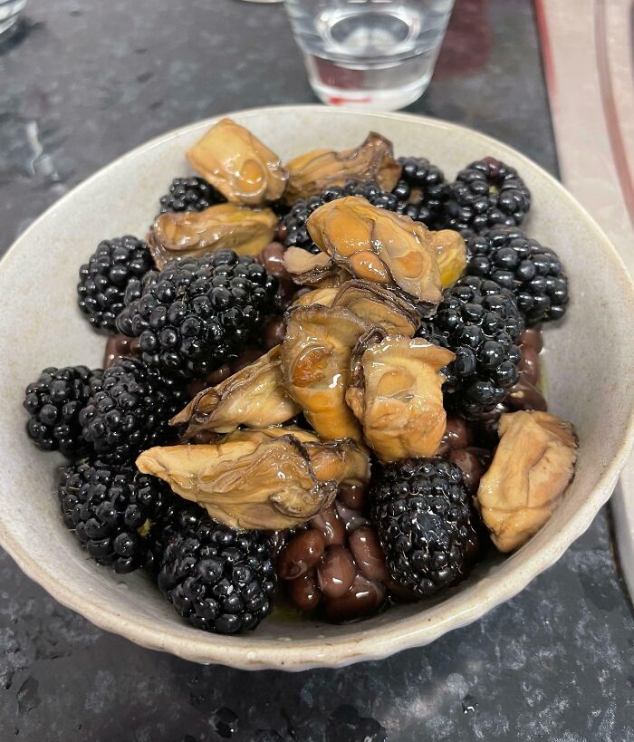 Bowl of unusual combination of blackberries, beans, and slimy food pieces in a close-up cursed and disgusting food picture.