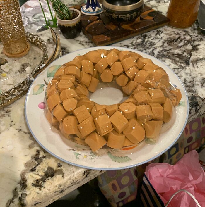 Ring of gelatin with cubed hot dogs inside on a plate, a cursed and disgusting food combination on a kitchen counter.