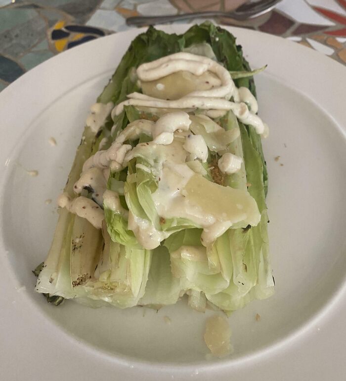 Grilled lettuce with uneven dressing and cheese on a white plate, a cursed and disgusting food presentation.