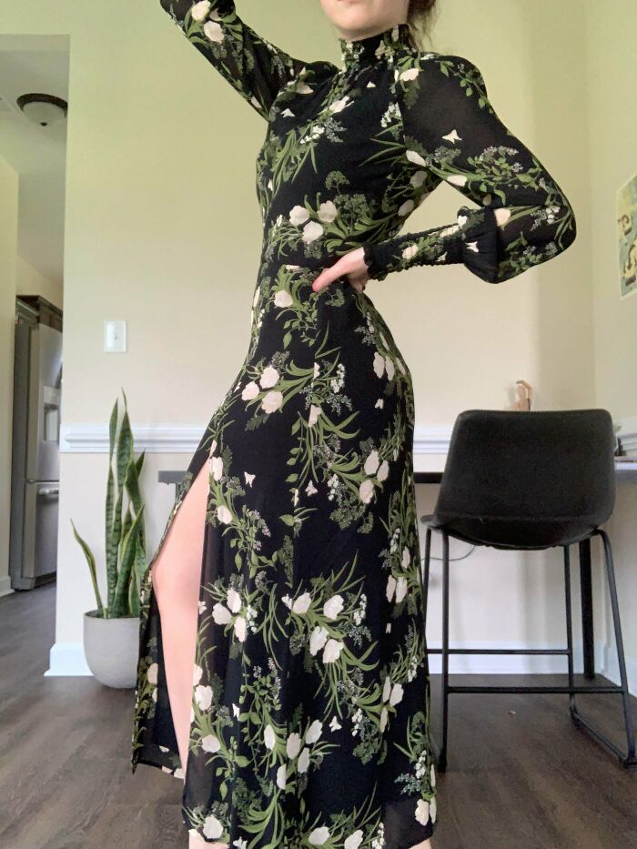 Person wearing a floral black dress with a high slit, showcasing a stylish thrift store fashion find indoors.