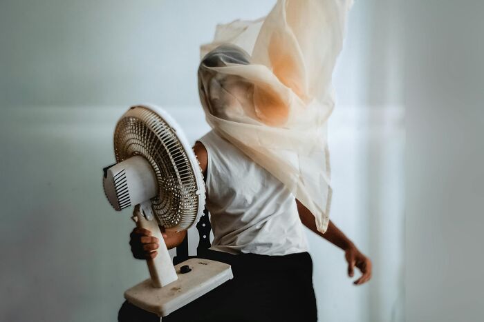 Person holding a fan with fabric blowing over their face, illustrating over-the-top workplace rules annoying everyone.