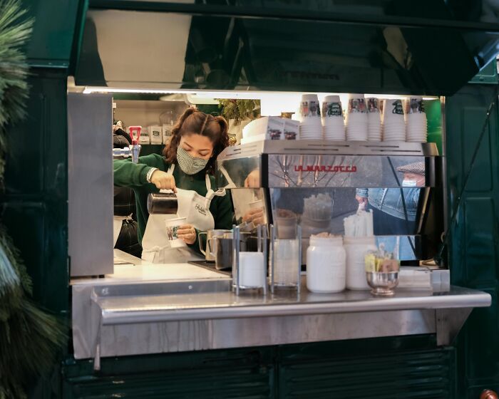 Barista wearing a mask preparing coffee behind a counter, illustrating workplace rules that annoyed employees.
