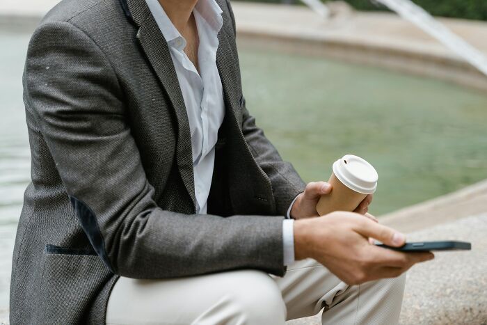 Man in blazer holding coffee cup and phone outdoors, illustrating workplace rules that annoyed employees.