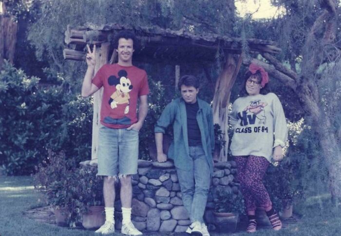 Three people in vintage 1980s clothing posing outdoors by a stone well, capturing wild, weird, and wonderful 1980s style.