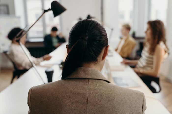 Person facing coworkers in a meeting room, illustrating workplace rules that are over-the-top and annoy employees.